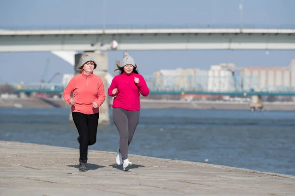 Madre e hija usando ropa deportiva y corriendo en el día ventoso —  Fotos de Stock