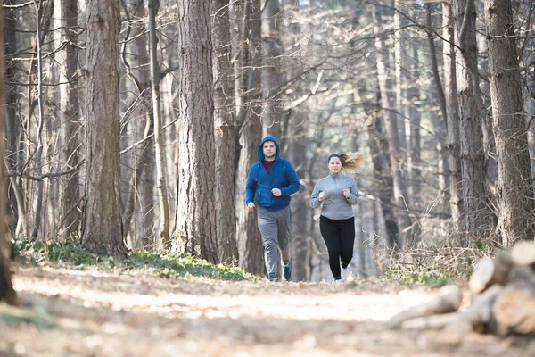 Ragazza e giovane uomo che indossa abbigliamento sportivo e correre nella foresta a m — Foto Stock