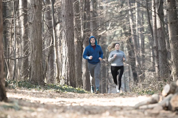 Ragazza e giovane uomo che indossa abbigliamento sportivo e correre nella foresta a m — Foto Stock