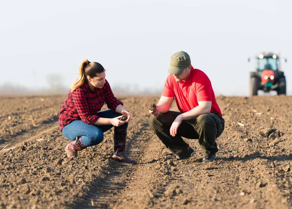 Jovens agricultores examinando sujeira enquanto trator é arar campos — Fotografia de Stock
