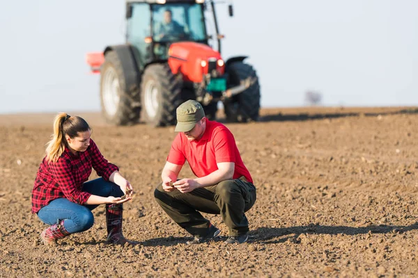 Jovens agricultores examinando sujeira enquanto trator é arar campos — Fotografia de Stock