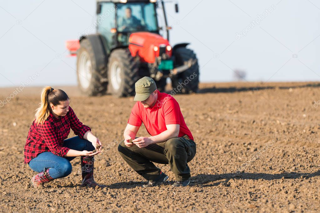 Young farmers examing  dirt while tractor is plowing fields