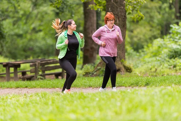 Mother and daughter wearing sportswear and running in forest at — Stock Photo, Image