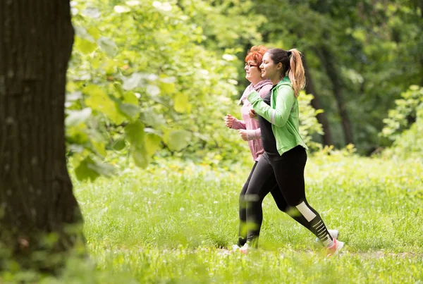 Madre e figlia indossando abbigliamento sportivo e correndo nella foresta a — Foto Stock
