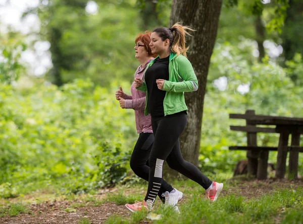 Mother and daughter wearing sportswear and running in forest at — Stock Photo, Image
