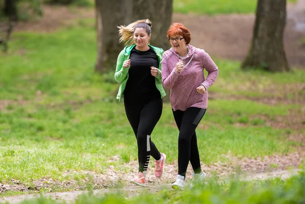 Madre e figlia indossando abbigliamento sportivo e correndo nella foresta a — Foto Stock