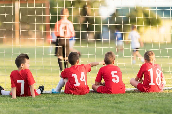 Joueurs de football enfants assis derrière le but regarder le match de football — Photo