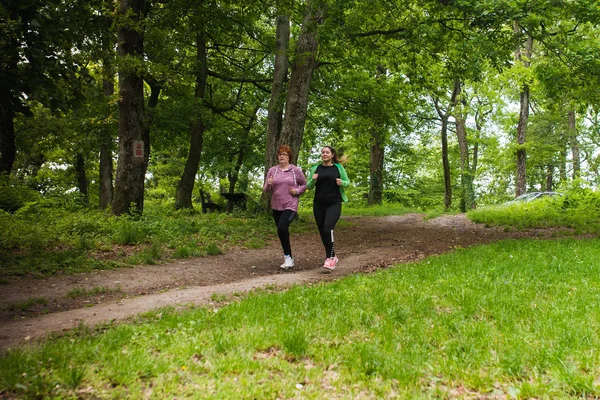 Mother and daughter wearing sportswear and running in forest at — Stock Photo, Image