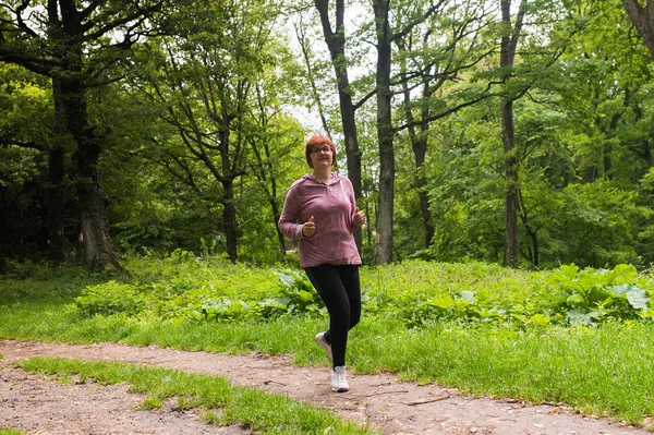 Ältere Frau in Sportkleidung läuft im Wald am Berg — Stockfoto