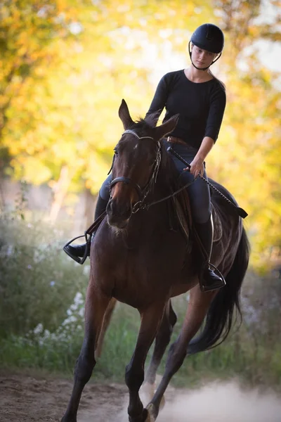 Jeune jolie fille chevauchant un cheval avec des feuilles rétroéclairées derrière — Photo