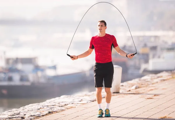 Young man wearing sportswear skipping rope at quay during autumn — Stock Photo, Image