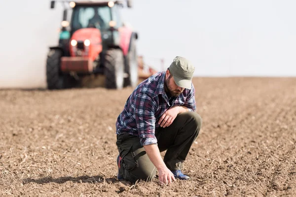 Mladý zemědělec kontrole špína zatímco traktor orat pole — Stock fotografie