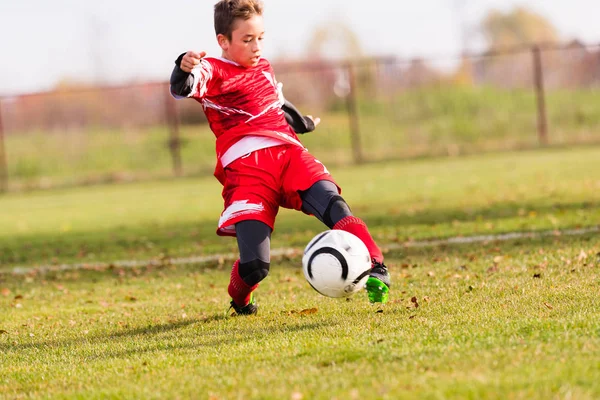 Pojken sparkar fotboll på idrottsplatsen — Stockfoto