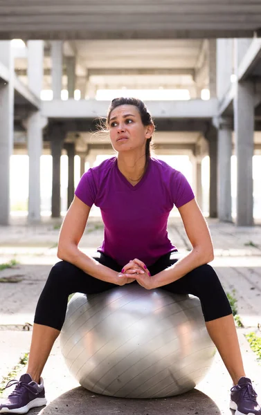 Young beautiful athlete girl  sitting on silver pilates ball  in — Stock Photo, Image