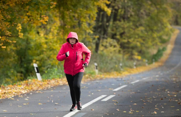 Keski-ikäinen nainen yllään urheiluvaatteet ja käynnissä metsässä . — kuvapankkivalokuva