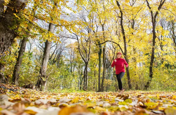 Donna di mezza età che indossa abbigliamento sportivo e corre nella foresta . — Foto Stock