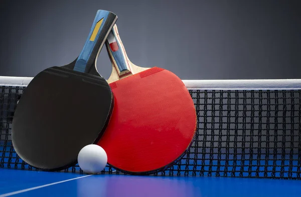 Tischtennisschläger und Bälle auf einem blauen Tisch mit Netz. — Stockfoto