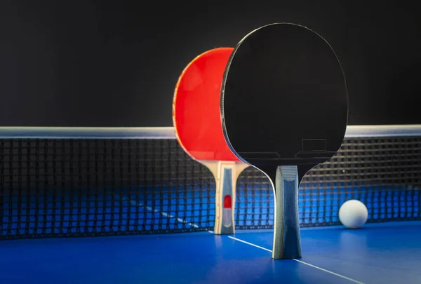 Tischtennisschläger und Bälle auf einem blauen Tisch mit Netz. — Stockfoto