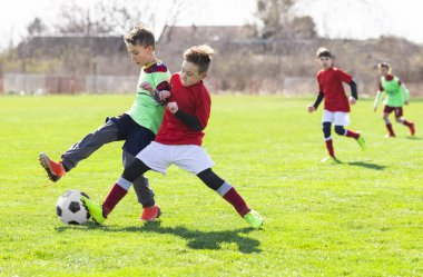 Çocuklar sahada futbol oynuyor.