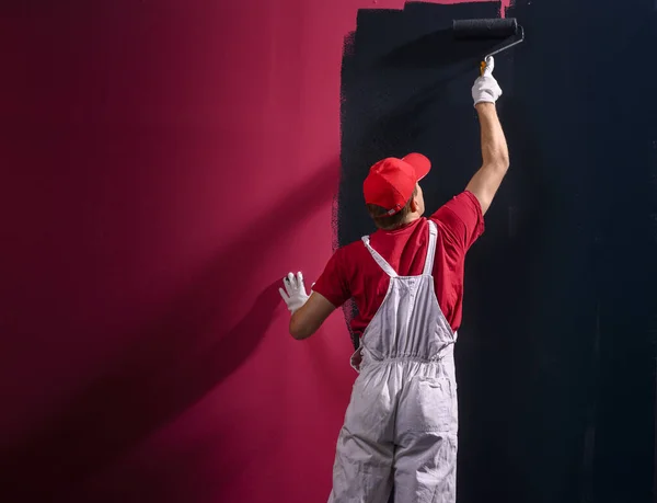 Man painting a wall. Painter in red overall painting wall in black color