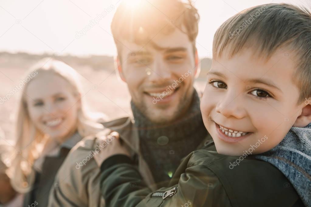 Happy family hugging with son on seashore in autumn with backlit
