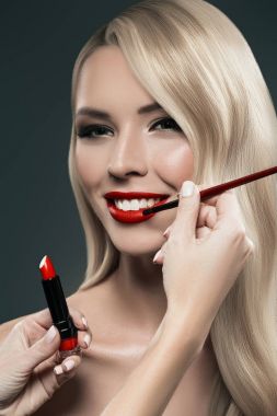Güzel sarı saçlı kız visagiste ile portre siyah izole fırça ile uygulanan ruj eller
