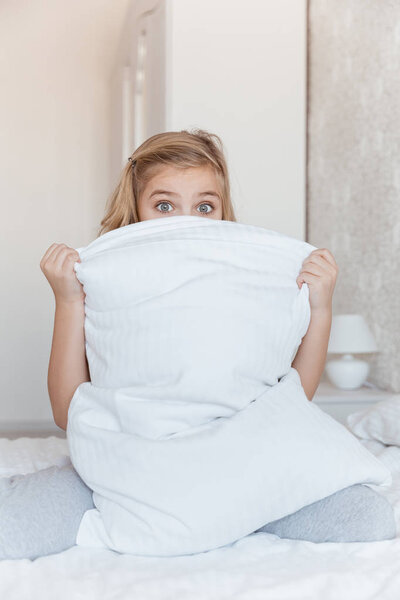 surprised kid sitting on bed and looking out from pillow