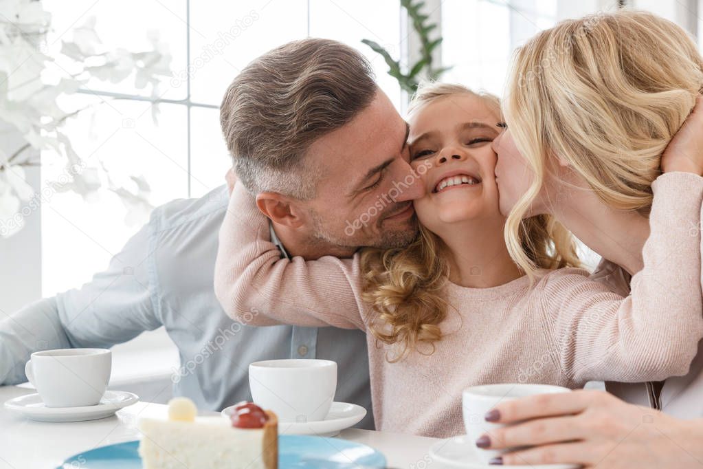 Parens kissing their daughter while spending time in cafe together