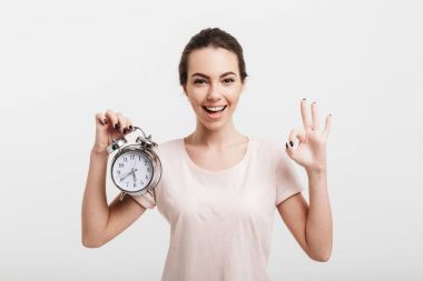 beautiful girl showing ok gesture and holding alarm clock isolated on white clipart