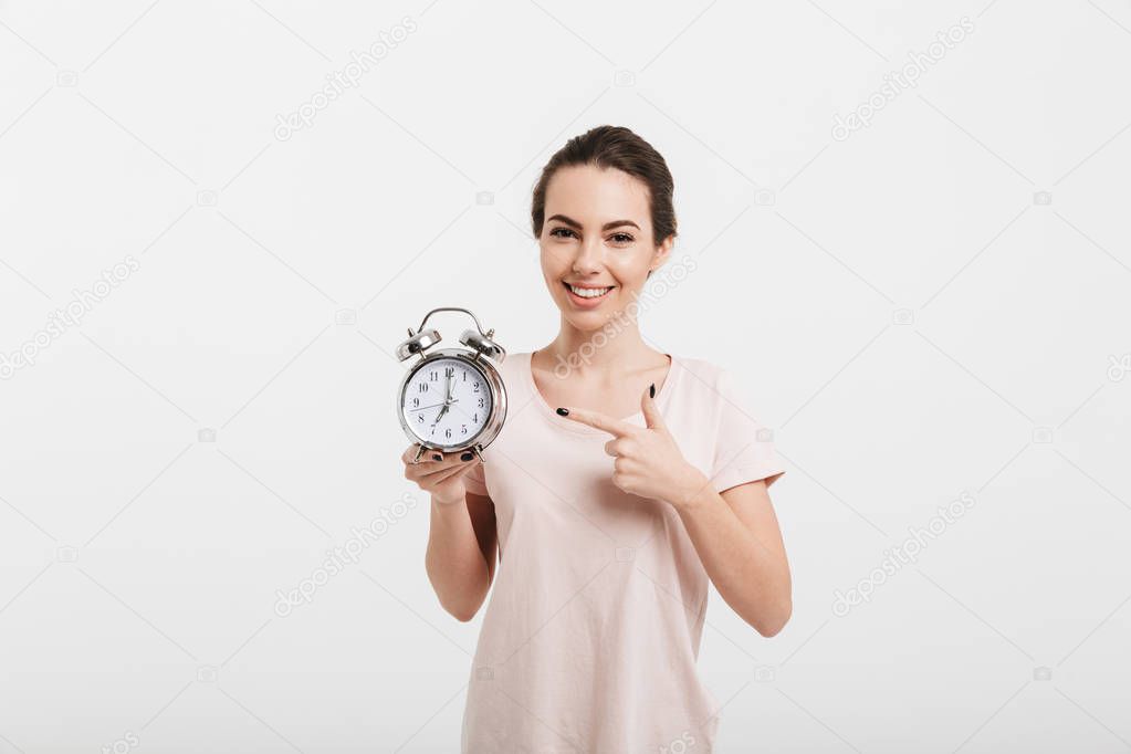 smiling girl pointing on alarm clock isolated on white