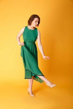 Turuncu üzerinde izole ayakkabı bakarak yeşil elbiseli genç güzel kadın