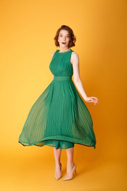 Turuncu üzerinde izole yeşil elbiseli genç güzel kadın