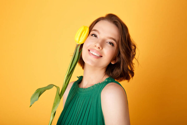 portrait of smiling woman with yellow tulip isolated on orange
