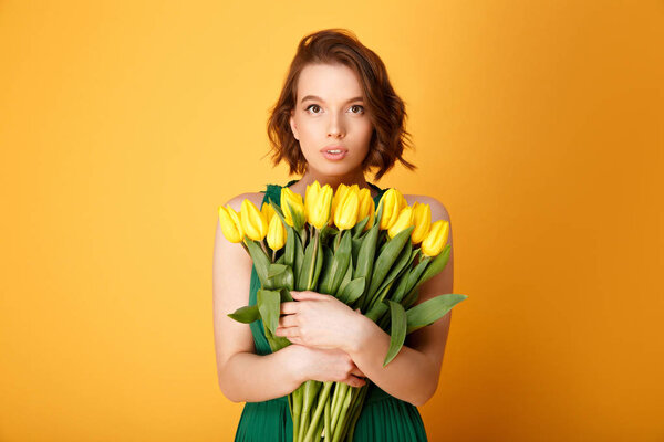 portrait of beautiful woman with bouquet of yellow tulips isolated on orange