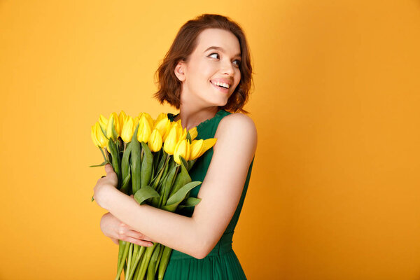 portrait of smiling woman with bouquet of yellow tulips isolated on orange