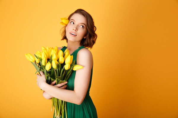 portrait of young pretty woman with bouquet of yellow tulips isolated on orange
