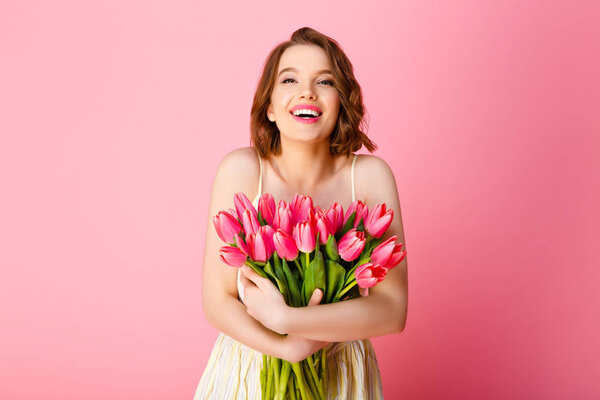 portrait of happy woman in white dress with bouquet of spring tulips isolated on pink