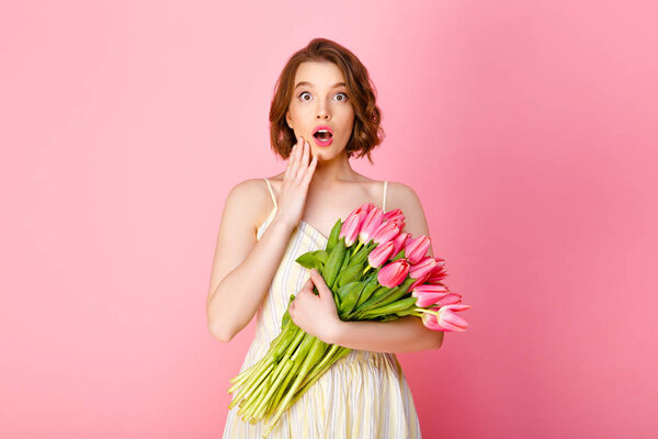 surprised woman with bouquet of pink tulips isolated on pink