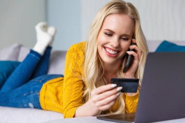 güzel genç kadın holding kredi kartı gülümseyen ve smartphone tarafından evde konuşmak