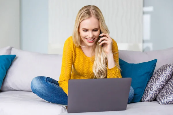 Mooie Lachende Blond Meisje Met Laptop Praten Door Smartphone Thuis — Gratis stockfoto