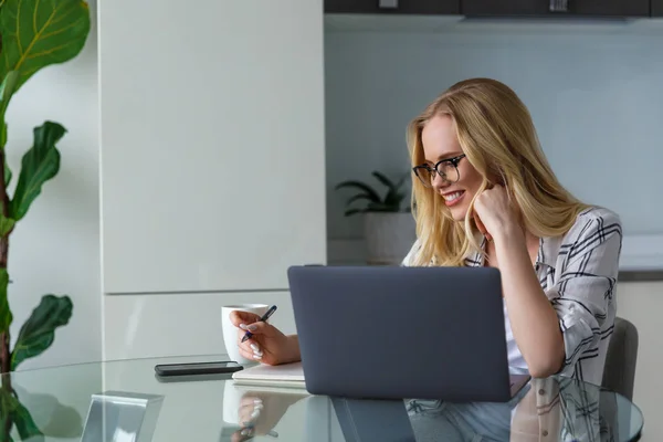 Wanita Muda Tersenyum Dalam Kacamata Menggunakan Laptop Dan Mengambil Catatan — Stok Foto