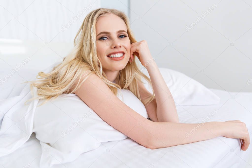 beautiful young blonde woman lying on bed and smiling at camera