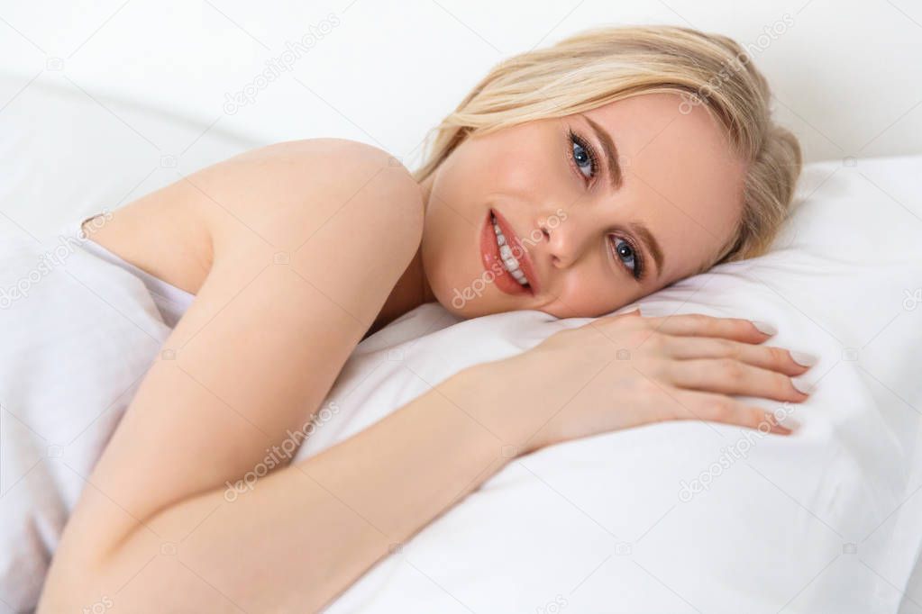 beautiful young woman smiling at camera while lying in bed