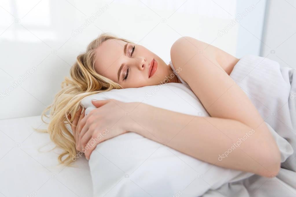 beautiful young blonde woman sleeping on white pillow in bed