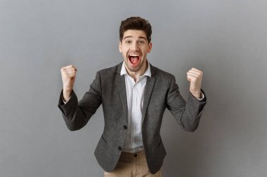 portrait of excited businessman gesturing and looking at camera against grey wall background clipart