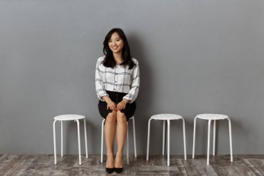 smiling asian businesswoman sitting on chair while waiting for job interview clipart