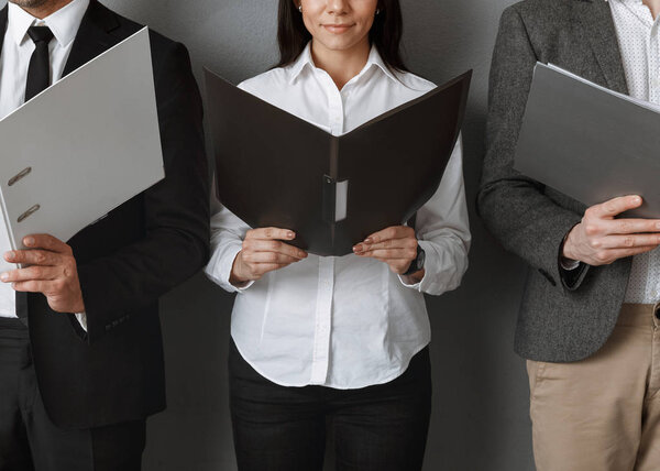 partial view of business colleagues with folders against grey wall