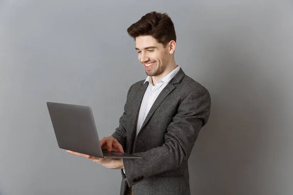 Sonriente Hombre Negocios Traje Usando Portátil Contra Fondo Pared Gris —  Fotos de Stock