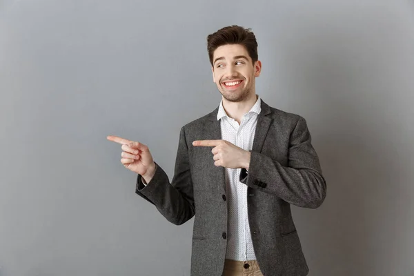 Portrait Smiling Businessman Suit Pointing Away Grey Wall — Stock Photo, Image