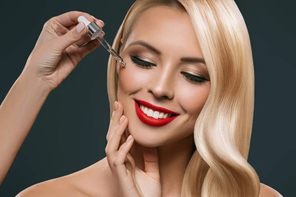 Schöne blonde Mädchen Anwendung Behandlung von Pipette auf Gesicht, isoliert auf schwarz — Stockfoto